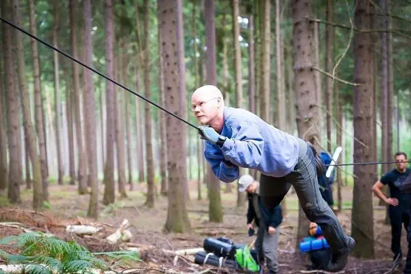 Mann überquert selbstgebaute Seilbrücke zwischen Bäumen im Wald