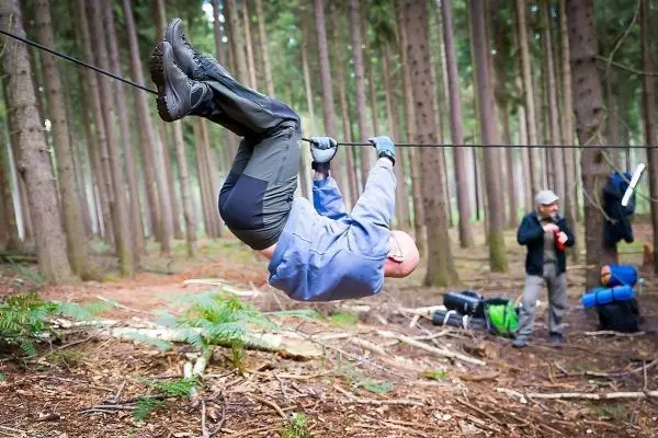 Mann überquert selbstgebaute Seilbrücke zwischen Bäumen im Wald