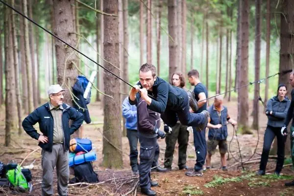 Mann überquert selbstgebaute Seilbrücke zwischen Bäumen im Wald