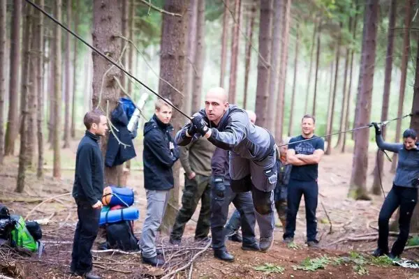 Mann überquert selbstgebaute Seilbrücke zwischen Bäumen im Wald