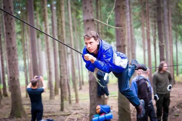 Mann überquert selbstgebaute Seilbrücke zwischen Bäumen im Wald