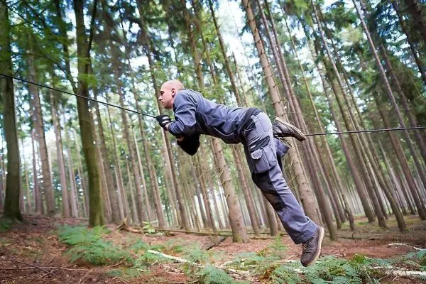 Mann überquert selbstgebaute Seilbrücke zwischen Bäumen im Wald