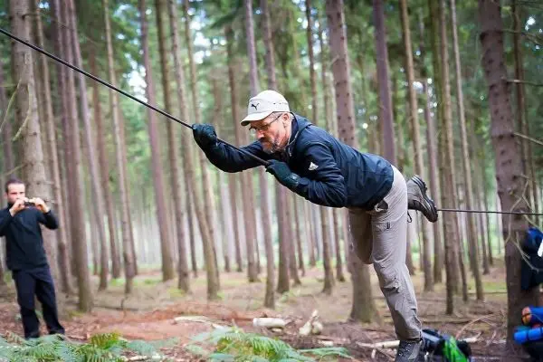 Mann überquert selbstgebaute Seilbrücke zwischen Bäumen im Wald