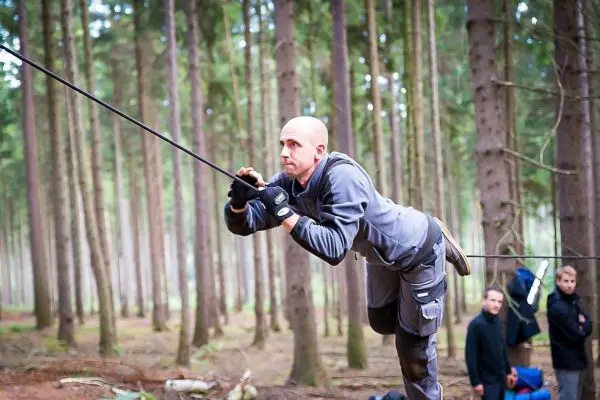 Mann überquert selbstgebaute Seilbrücke zwischen Bäumen im Wald