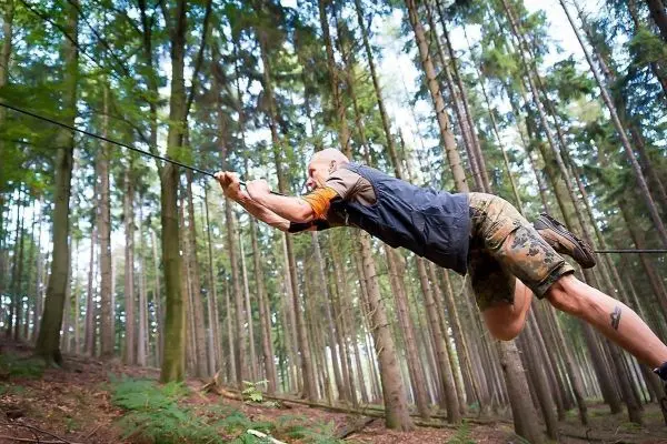 Mann überquert selbstgebaute Seilbrücke zwischen Bäumen im Wald