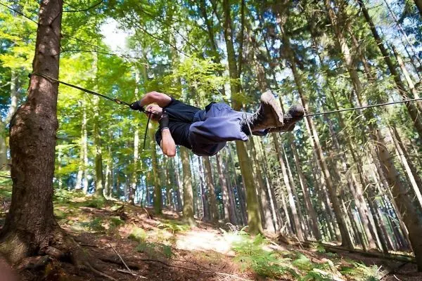 Mann überquert selbstgebaute Seilbrücke zwischen zwei Bäumen im Wald