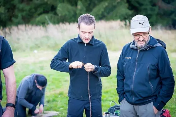 Messer bearbeitet Holzstück, während zwei Personen beobachten