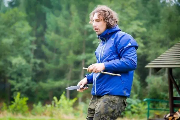 Messer in der Hand, hält ein Stockstück zum Bearbeiten