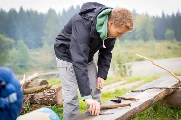 Messer und Holzstücke liegen auf einem Baumstamm, während jemand daran arbeitet