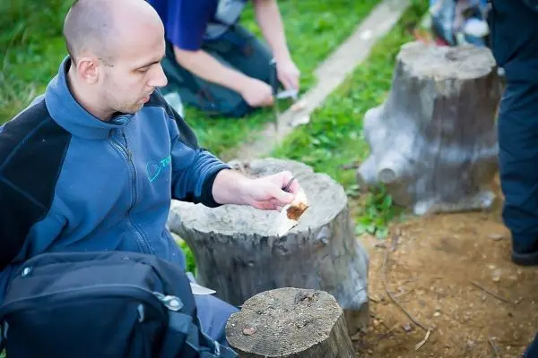 Person hält ein Stück Holz und sitzt auf einem Baumstumpf beim Überlebenstraining
