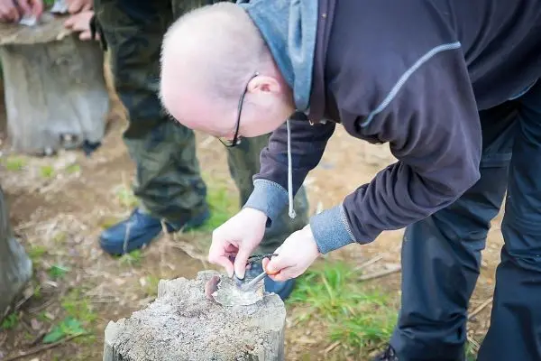 Person schnitzt mit einem Messer auf einem Baumstumpf