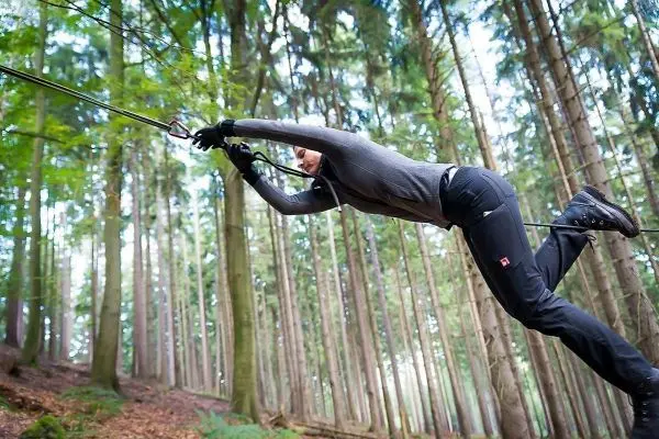 Person schwingt an Seil zwischen Bäumen im Wald