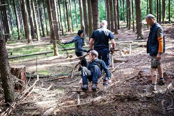 Person sitzt auf dem Boden, andere Personen stehen im Wald