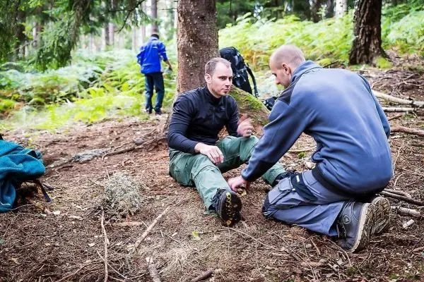 Person sitzt auf dem Boden und erhält Hilfe von einer anderen Person beim Überlebenstraining