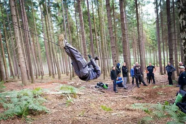 Person überquert selbstgebaute Seilbrücke zwischen Bäumen im Wald