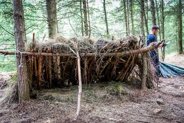 Selbstgebaute Tarp-Notunterkunft aus Ästen und Gras im Wald