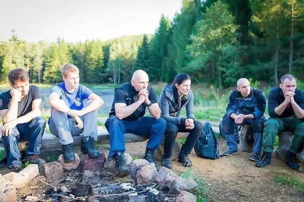 Sitzende Personen um ein kleines Bodenfeuer in einer Waldumgebung
