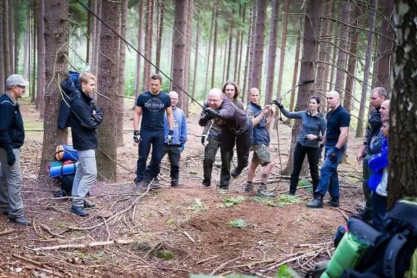Teilnehmer überqueren eine selbstgebaute Seilbrücke im Wald