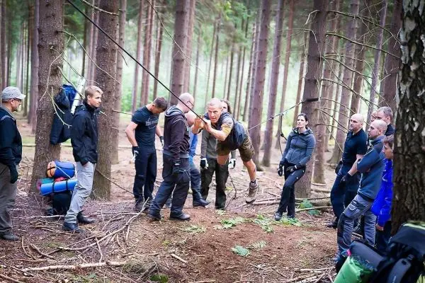 Teilnehmer überqueren eine selbstgebaute Seilbrücke zwischen zwei Bäumen