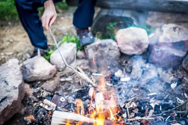 Zunder glimmt in einem kleinen Bodenfeuer, während ein Stock gehalten wird
