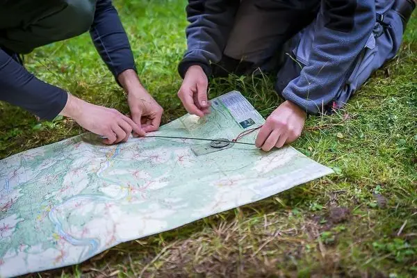 Zwei Hände legen einen Kompass auf eine Landkarte auf dem Boden