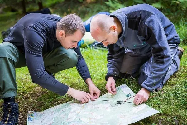 Zwei Personen analysieren eine Karte auf dem Boden im Wald