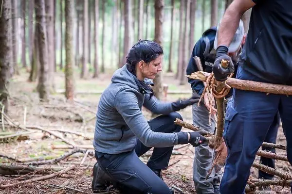 Zwei Personen bauen eine Holzstruktur im Wald mit Ästen und Seil