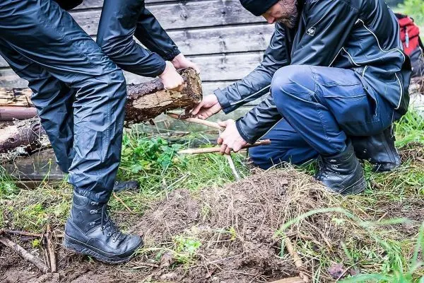 Zwei Personen bearbeiten einen Holzstamm mit einem Messer auf dem Boden