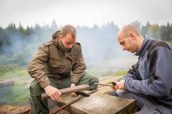 Zwei Personen bearbeiten Holzstücke auf einem Tisch im Freien