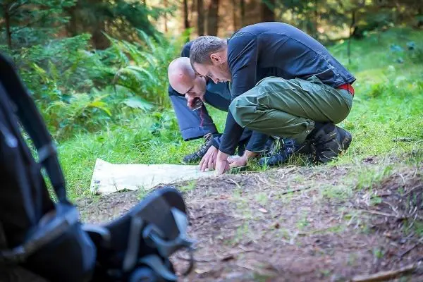 Zwei Personen betrachten eine Karte auf dem Boden im Wald