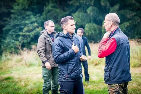 Zwei Personen im Gespräch, weitere Teilnehmer im Hintergrund auf einer Wiese