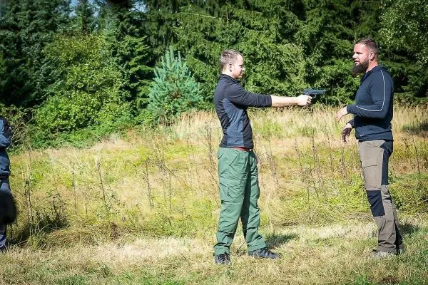 Zwei Personen in einem Feld, eine Person hält eine Pistole auf die andere
