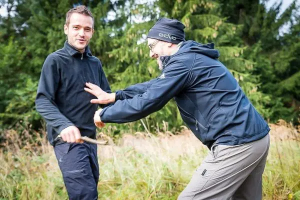Zwei Personen interagieren im Freien, eine hält einen Stock in der Hand