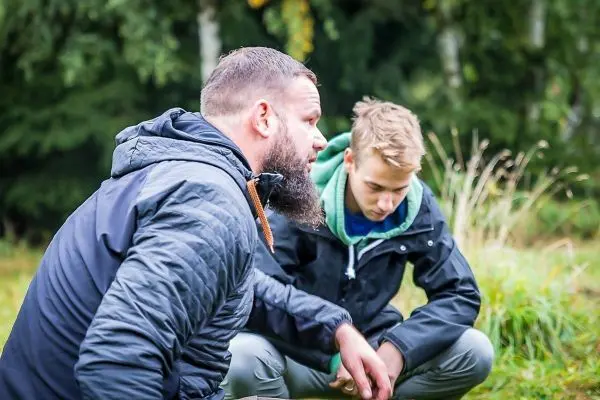 Zwei Personen knien im Gras und sprechen miteinander