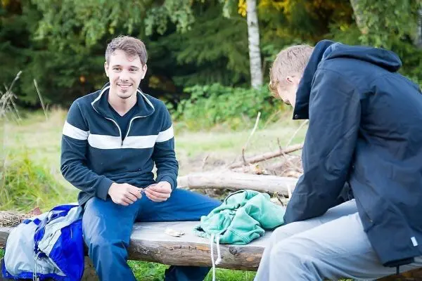 Zwei Personen sitzen auf einem Baumstamm und bereiten Ausrüstung vor