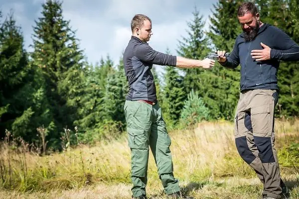 Zwei Personen stehen in einer Wiese und führen eine Übung mit einem Messer durch