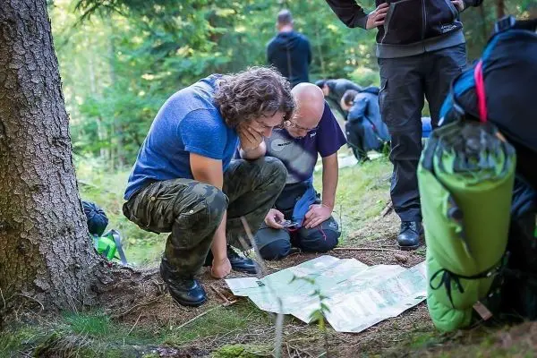 Zwei Personen studieren eine Karte im Wald, Rucksäcke liegen im Hintergrund