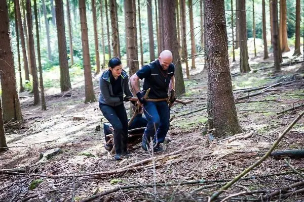 Zwei Personen tragen eine improvisierte Trage durch den Wald
