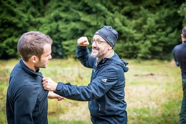 Zwei Personen üben eine körperliche Technik im Freien, einer greift den anderen an