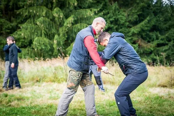 Zwei Personen üben eine Nahkampftechnik im Freien auf einer Wiese