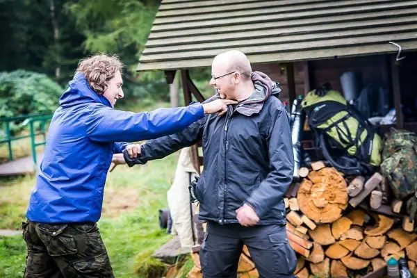 Zwei Personen üben eine Selbstverteidigungstechnik in der Nähe eines Holzstapels