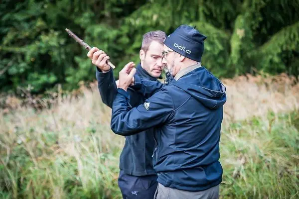 Zwei Personen üben eine Technik mit einem Stock in einer grasbewachsenen Umgebung