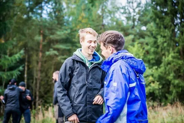 Zwei Personen unterhalten sich in einem Waldgebiet, umgeben von Bäumen