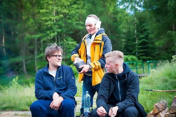 Drei Personen sitzen am Lagerplatz, eine Person steht mit einer Kanne in der Hand