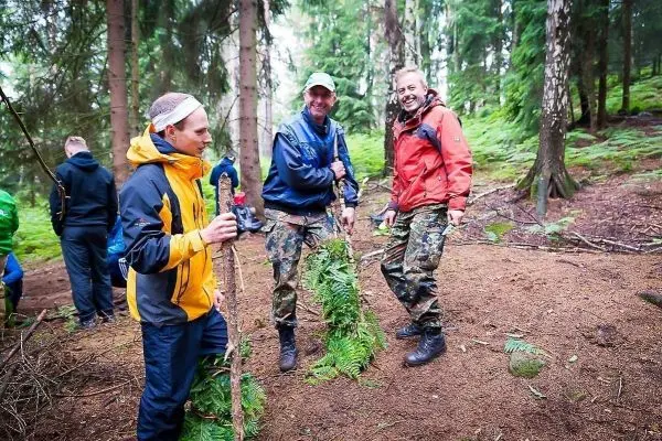 Drei Personen stehen im Wald und halten improvisierte Stöcke in der Hand
