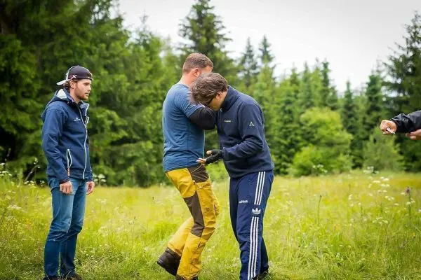 Drei Personen stehen in einer Wiese, eine Person wird gestützt