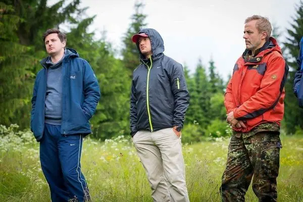 Drei Personen stehen in einer Wiese umgeben von Bäumen