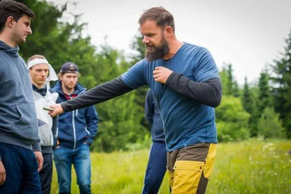 Ein Trainer demonstriert eine Technik im Freien, während Teilnehmer aufmerksam zuschauen
