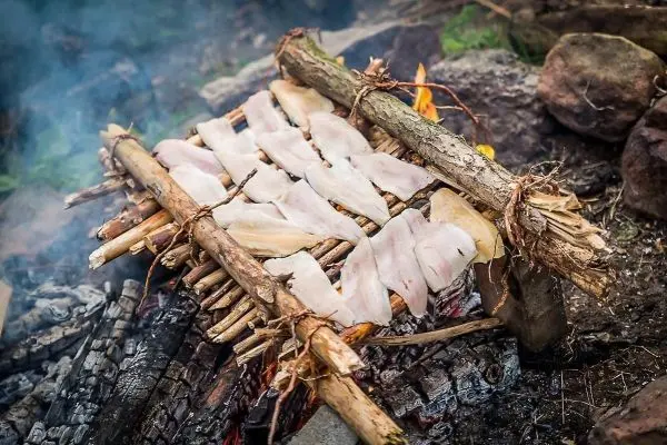 Fischfilets garen auf improvisierter Holzgrillkonstruktion über offenem Feuer