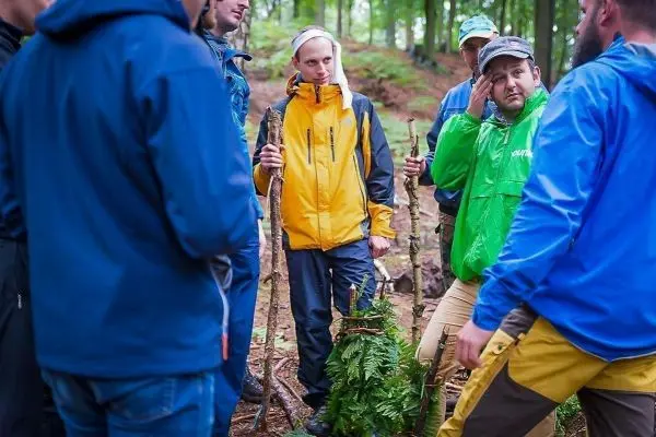 Gruppe diskutiert im Wald über Techniken mit Ästen und Pflanzen